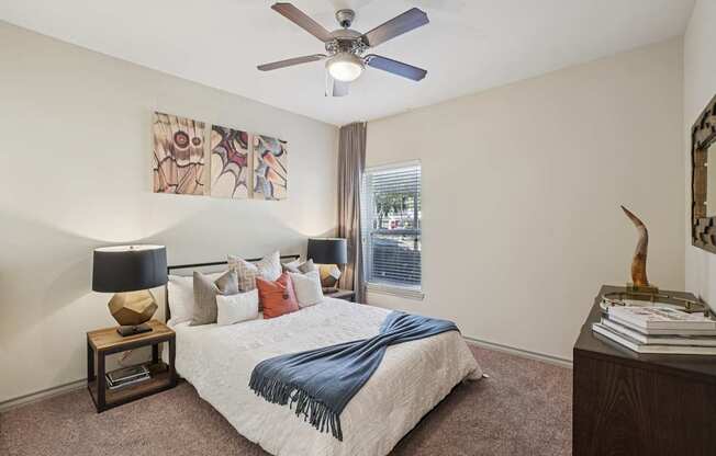 A bedroom with a bed, a ceiling fan, and a painting on the wall.