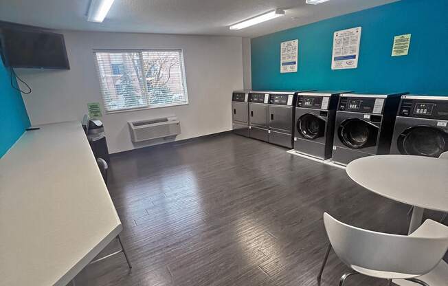 a laundry room with a row of washing machines and a table and chairs