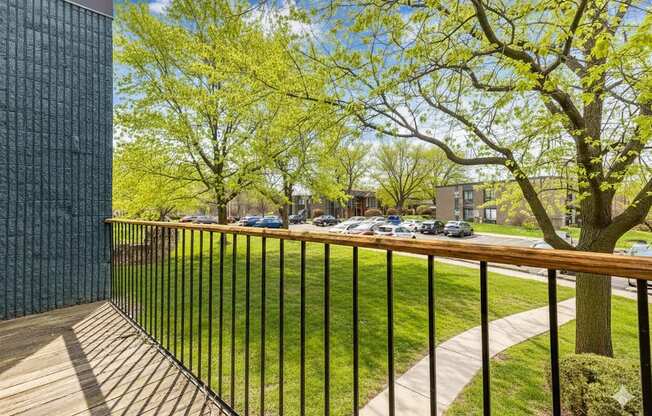 A balcony with a black railing and a view of a green lawn and trees.