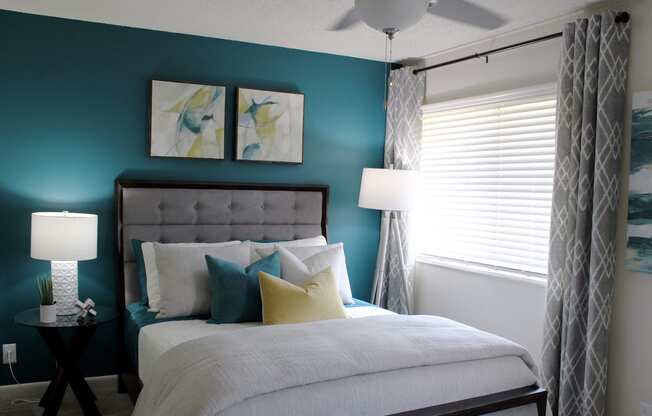 bedroom with large window, modern ceiling fan, teal accent wall and model furnishings  at Huntsville Landing Apartments, Huntsville, Alabama