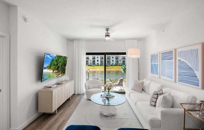 A living room with a television, a sofa, a coffee table, and a window overlooking a body of water.