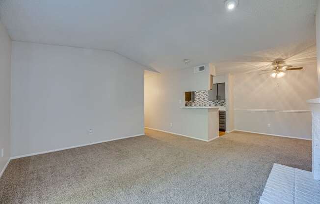 an empty living room with a ceiling fan and a kitchen