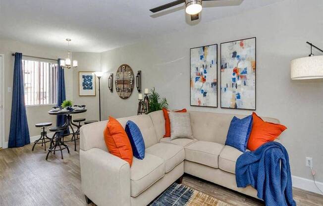 A living room with a beige couch, a ceiling fan, and a dining table with chairs.