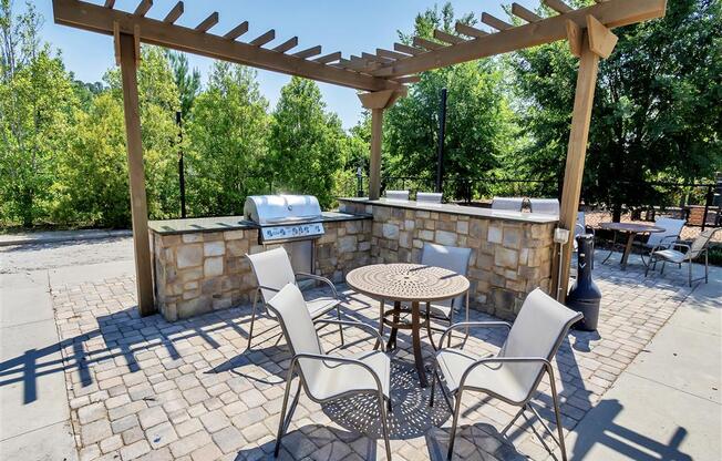 Grilling station with small wooden pergola, outdoor bar, and tables with chairs near trees