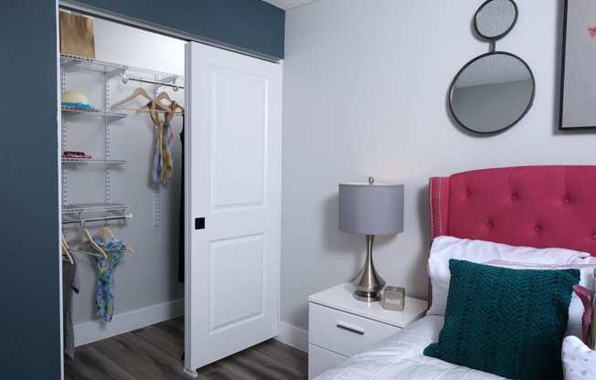 Fusion Las Vegas apartment closet white doors and built in wire shelving next to bed with hot pink headboard and teal crochet pillow.