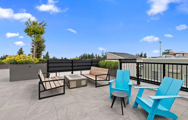 Two Blue Adirondack Chairs with two wooden benches facing cozy fireplace on the Resident Rooftop Lounge with a blue sky in the background at Arabella Apartment Homes, Shoreline, Washington 98155