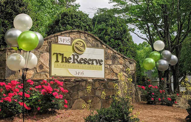 A sign for The Reserve surrounded by balloons and flowers.