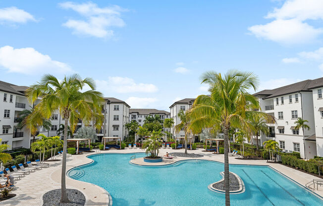 a large swimming pool with palm trees in front of some apartment buildings