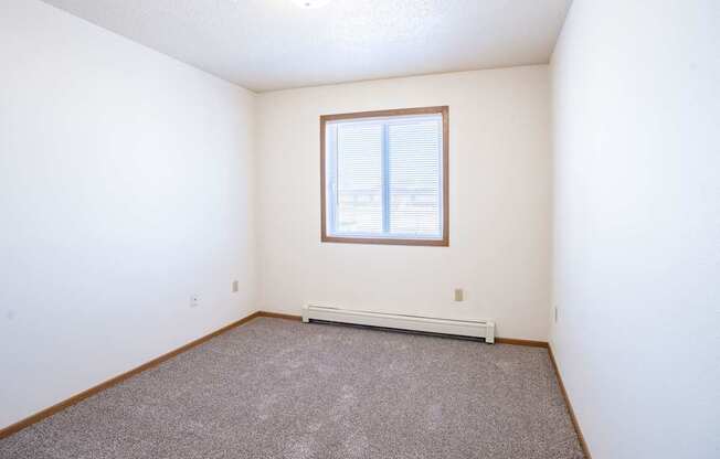 A room with a window and a carpeted floor. Fargo, ND Country Edge Apartments