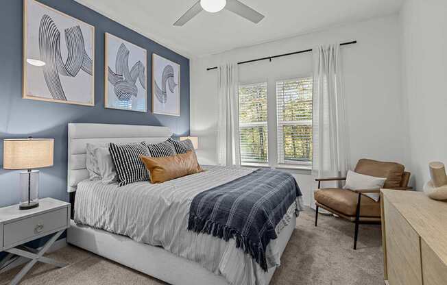 A bedroom with a bed, chair, and artwork on the wall.