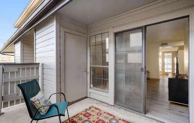 A chair with a cushion sits on a porch with a rug.