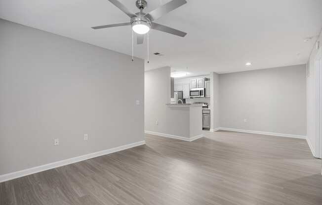 an empty living room with a ceiling fan and a kitchen