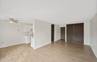 an empty living room and kitchen with wood flooring and a ceiling fan