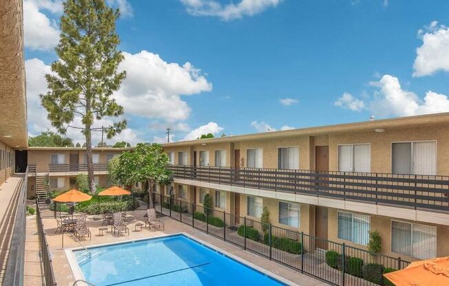 a hotel pool with umbrellas and tables and chairs at Villa La Paz Apartments, Bellflower, CA, 90706