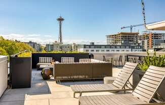 a rooftop patio with chairs and tables and a city in the background