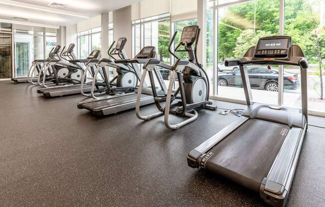 a gym with cardio equipment and large windows