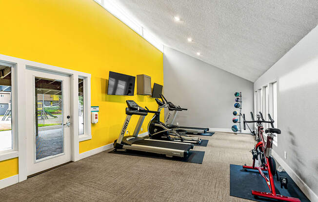 A bright yellow wall with a treadmill and exercise equipment in a room.