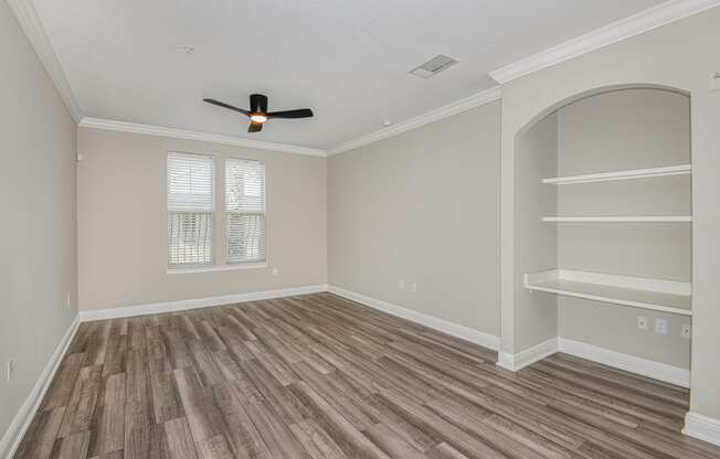 an empty bedroom with a ceiling fan and shelves