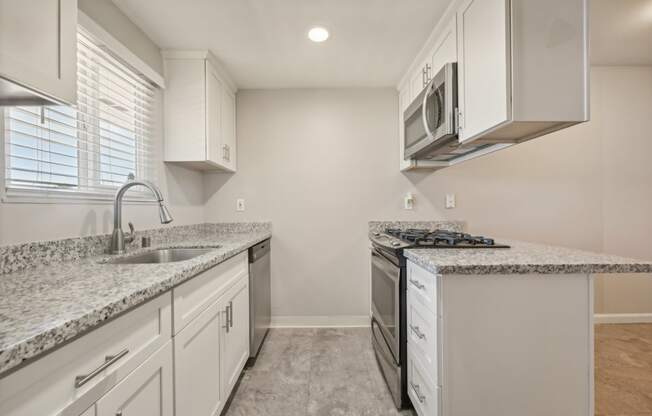 Fremont, CA, Apartments for Rent - Northgate Savoy - Kitchen with Granite Countertops, White Cabinetry, Stainless Steel Appliances, Tile Flooring, and a Large Window.