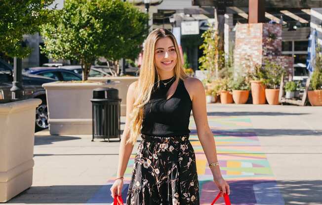 A woman in a black top and floral skirt is walking with shopping bags.