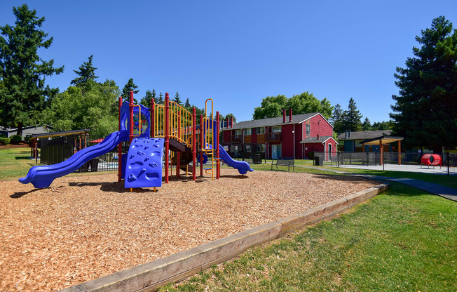 a playground with a blue slide and a red building in the background