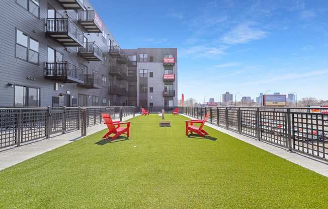 a grassy area with red chairs on a balcony of an apartment building