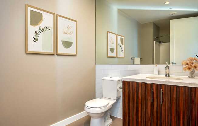 A bathroom with a toilet, sink, and framed pictures on the wall.