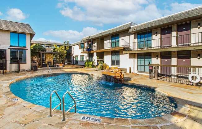 A swimming pool in front of a building with a stone border.