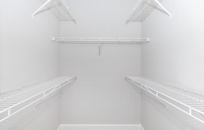 Empty walk-in closet featuring white wire shelving against light gray walls. The closet has multiple shelves, providing ample space for storage, and is carpeted. The overall look is clean and minimalist.
