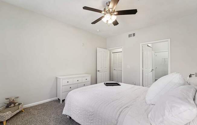 A white bedroom with a bed, dresser, and ceiling fan.