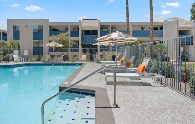 Pool with lounge chairs and striped umbrellas at The Halifax apartments in Phoenix, AZ.