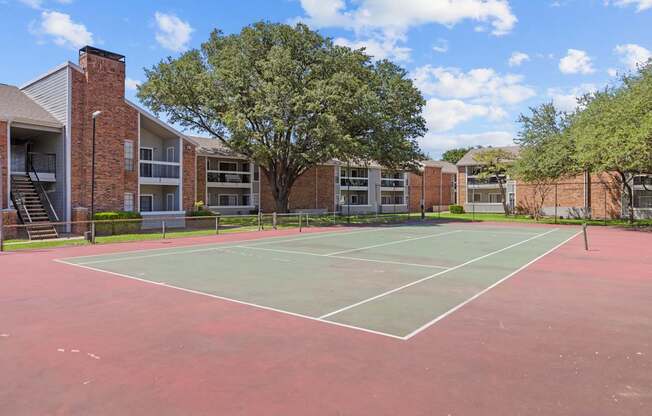 A tennis court is surrounded by apartment buildings.