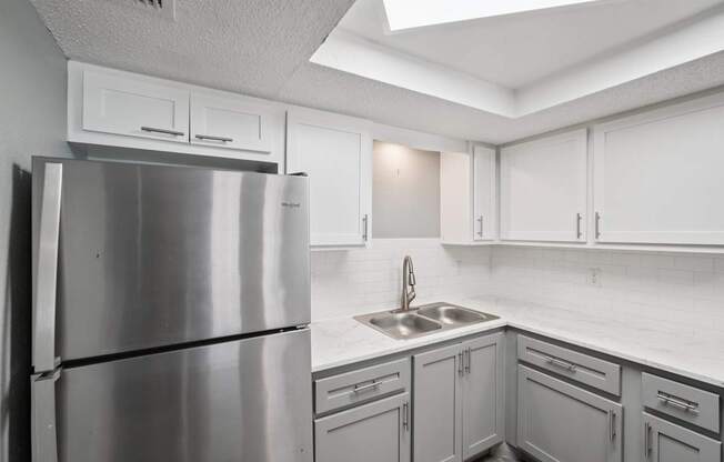 A kitchen with a stainless steel refrigerator and white cabinets.