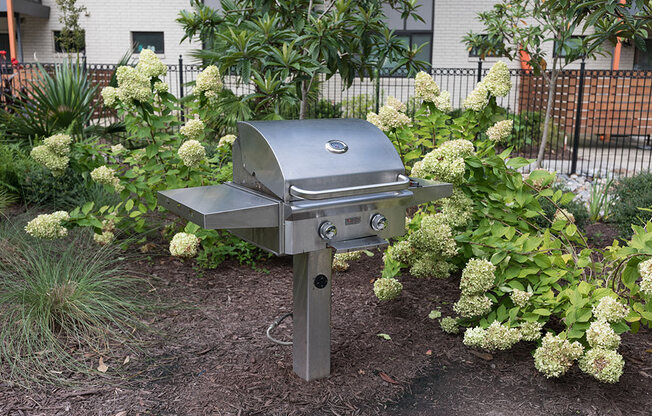 A silver barbecue grill is in the middle of a garden.
