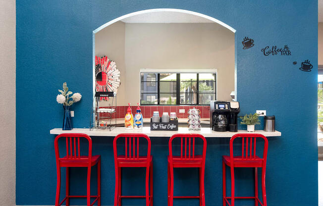a bar with four red stools in front of a counter with red chairs