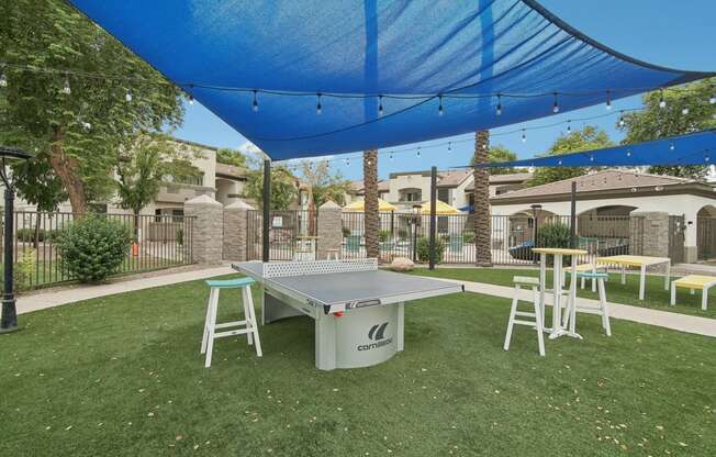 a ping pong table sits under a blue canopy in a yard