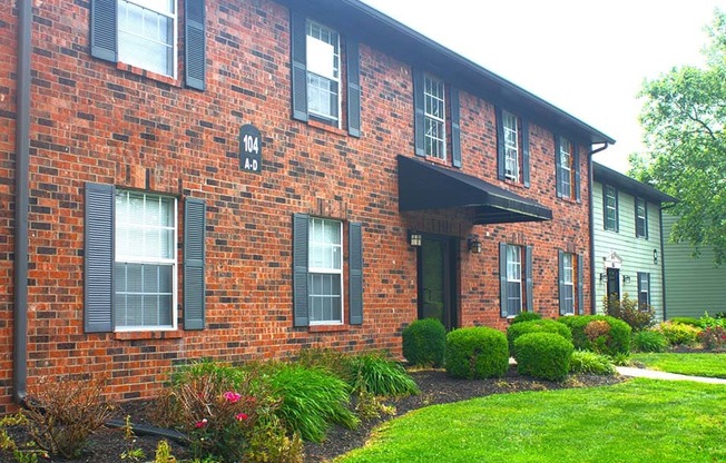 a brick apartment building with green grass and bushes in front of it