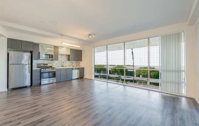 an empty living room with a kitchen and a large window