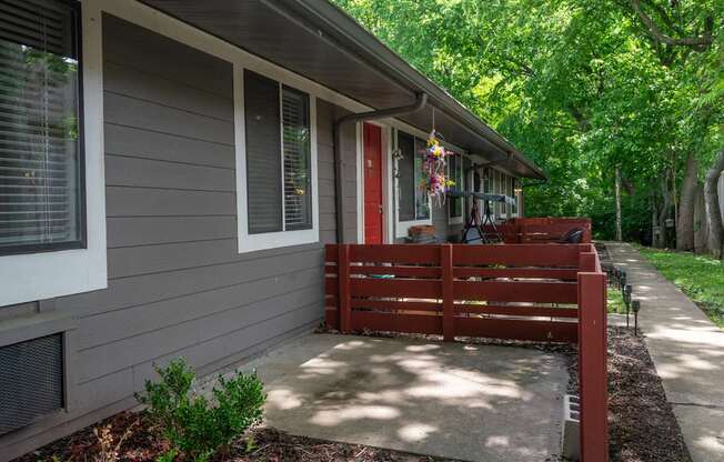A grey apartment at The Retreat Apartments with a red door and a red bench outside.