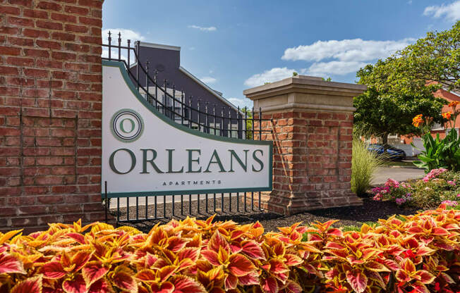 the sign for orleans apartments in front of a gate and flowers