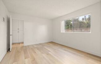 A room with wooden flooring and a window overlooking a fence.
