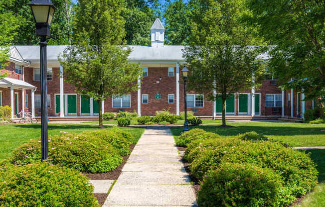 a brick building with green shutters and a lawn and trees in front of it at Nottingham Manor Apartments, Montvale, NJ, 07645