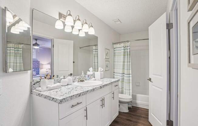A bathroom with a marble countertop and white cabinets.