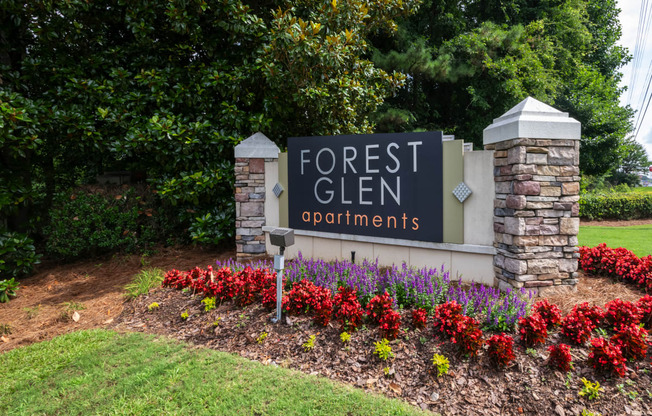 a sign for forest glen apartments in front of a flower garden
