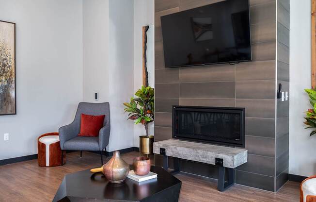 A grey chair with a red pillow sits in front of a grey wall with a flat screen TV mounted on it.