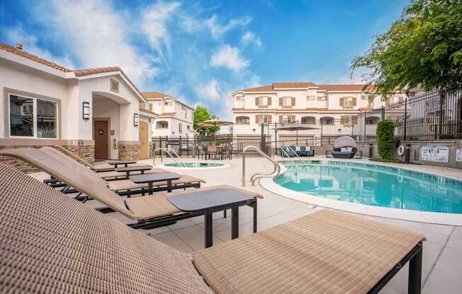 A pool area with sun loungers and a building in the background.