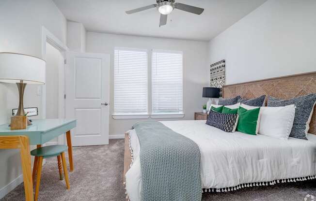 A bedroom with a bed, a table with a lamp, and a ceiling fan.