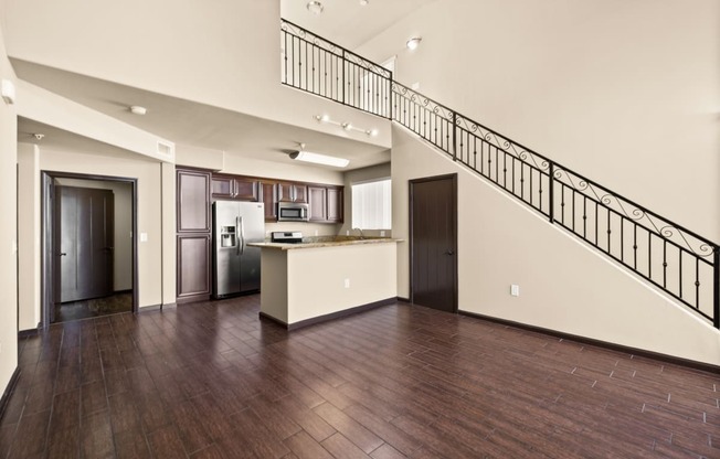 an empty living room with a staircase and a kitchen