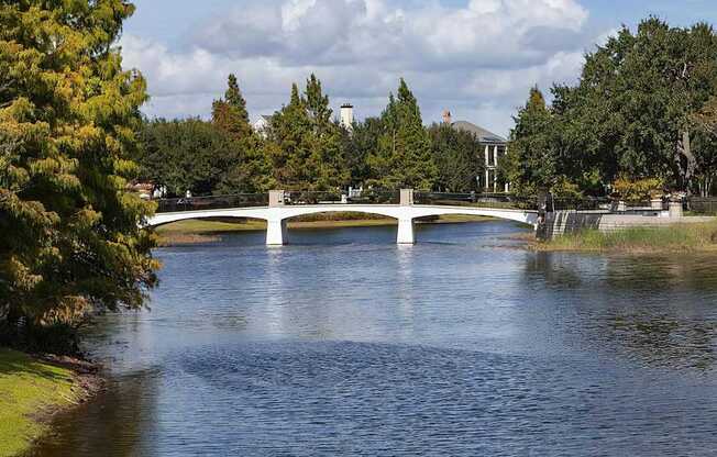 A white bridge over a calm body of water with trees on the left.