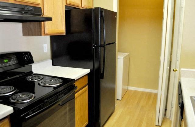 North Creek Apartments kitchen with black appliances, yellow hardwood floors, and laundry room behind